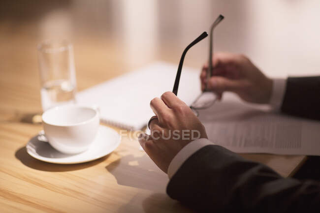 Businessman holding eyeglasses over paperwork — Stock Photo