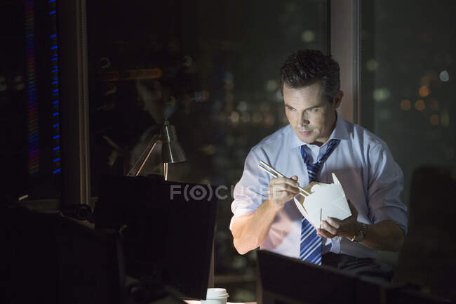 Businessman eating take out food in office at night — Stock Photo
