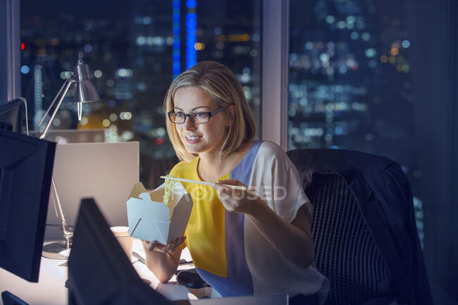 La donna d'affari che mangia tira fuori il cibo alla scrivania in ufficio di notte — Foto stock