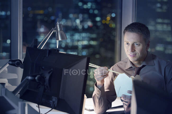 Homme d'affaires manger sortir de la nourriture à l'ordinateur portable dans le bureau la nuit — Photo de stock