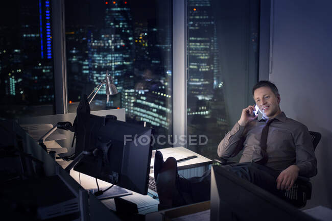 Empresario hablando por teléfono celular en la oficina por la noche - foto de stock