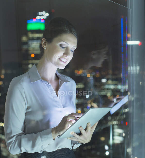Femme d'affaires utilisant une tablette numérique dans la fenêtre urbaine la nuit — Photo de stock