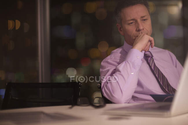 Серьезный бизнесмен, работающий допоздна за ноутбуком в офисе — стоковое фото