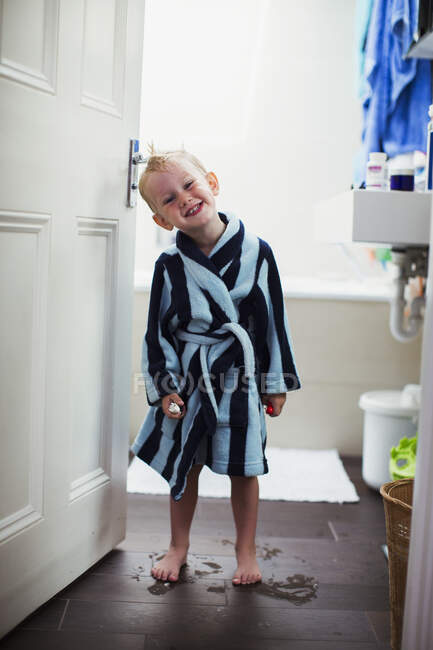 Niño en albornoz de pie en el baño goteando agua - foto de stock