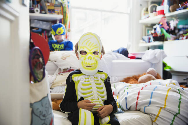 Junge sitzt im Skelett-Kostüm auf Bett in seinem Zimmer — Stockfoto