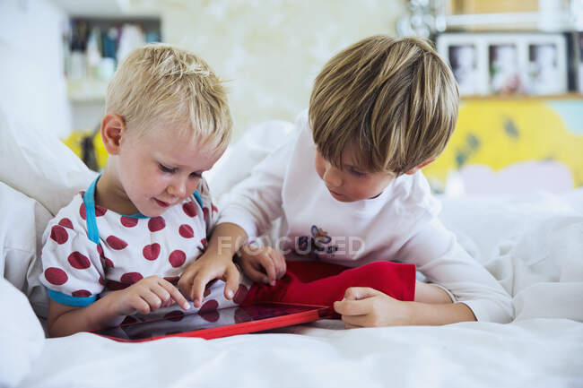Bothers playing with tablet in bed — Stock Photo