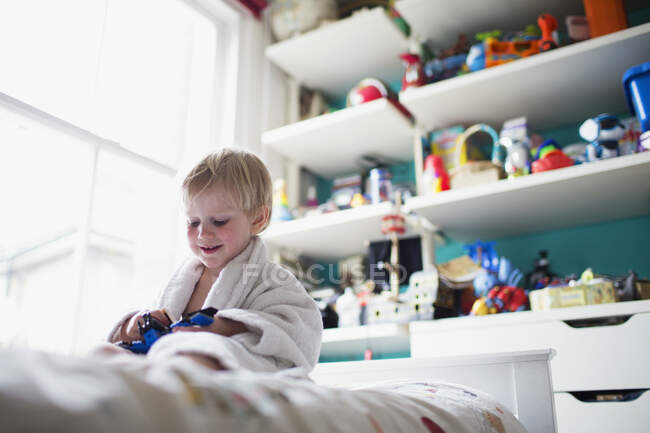Menino sentado na cama em seu quarto brincando com brinquedo — Fotografia de Stock