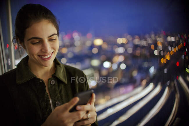 Усміхнена бізнес-леді зі смартфоном працює пізно в офісному вікні — стокове фото