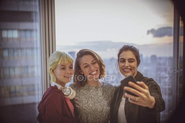 Улыбающиеся деловые женщины, делающие селфи у окна высотного офиса — стоковое фото