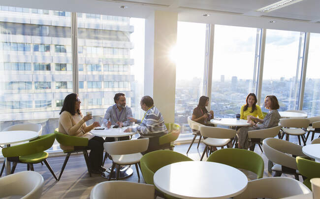 Geschäftsleute essen in sonniger Hochhaus-Cafeteria zu Mittag und unterhalten sich — Stockfoto