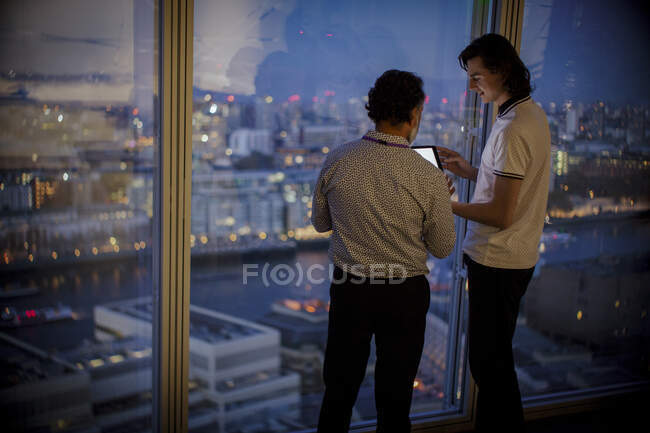 Бизнесмены с цифровым планшетом работают допоздна у окна высотного офиса — стоковое фото