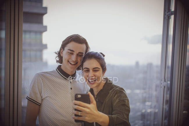 Feliz joven pareja tomando selfie en highrise ventana - foto de stock