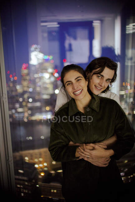 Portrait happy young couple hugging at highrise window — Stock Photo