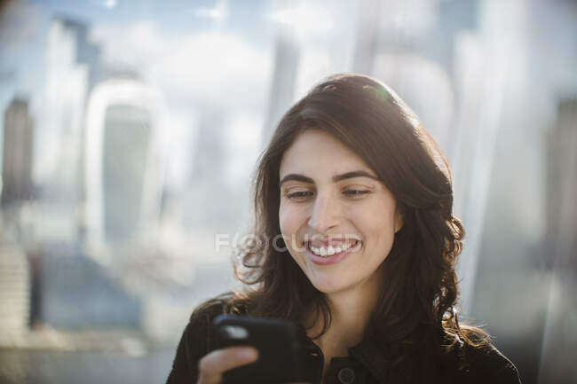 Улыбающаяся деловая женщина, использующая смартфон в солнечном окне — стоковое фото