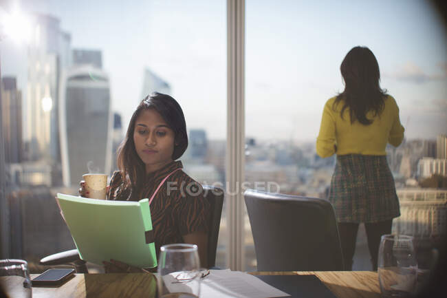 Businesswoman with coffee reviewing paperwork in conference room — Stock Photo