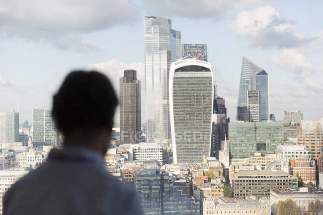 Hombre de negocios mirando el soleado paisaje urbano de Londres desde la ventana de la oficina, Reino Unido - foto de stock
