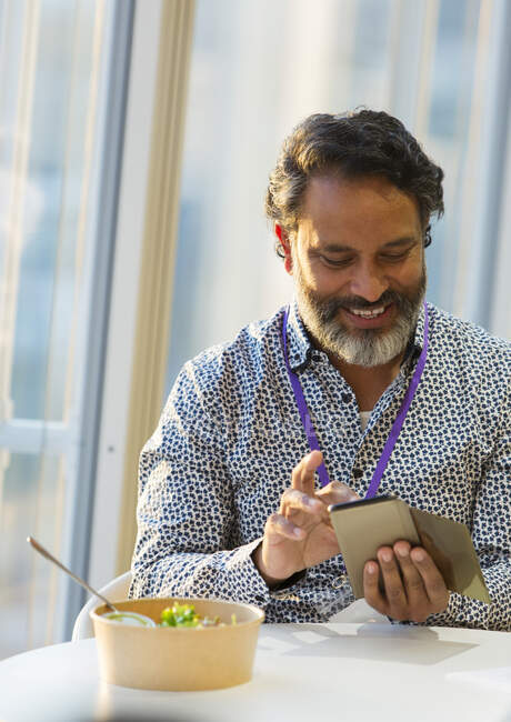 Hombre de negocios sonriente usando el teléfono inteligente en el almuerzo - foto de stock