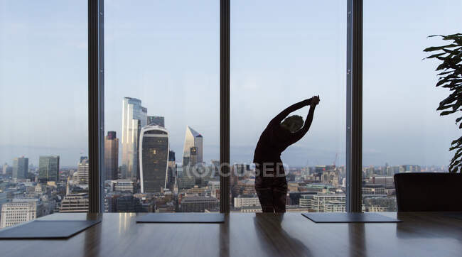 Femme d'affaires qui s'étire à la fenêtre du bureau Highrise, Londres, Royaume-Uni — Photo de stock