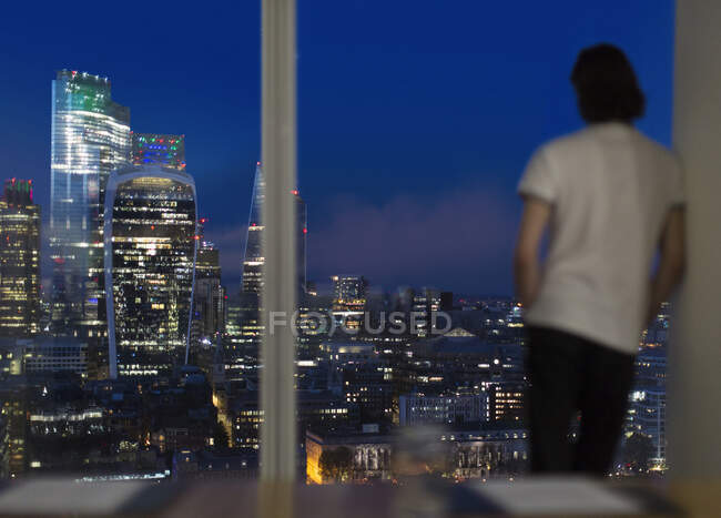 Бизнесмен, работающий поздним вечером у окна высотного офиса, Лондон, Великобритания — стоковое фото