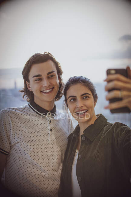 Happy young couple taking selfie with camera phone at window — Stock Photo