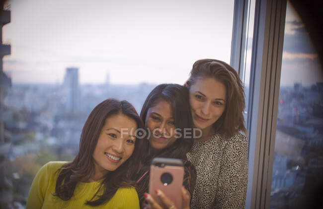 Businesswomen taking selfie with smart phone at highrise office window — Stock Photo