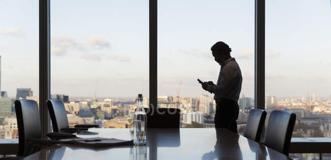 Бизнесмен с помощью смартфона у окна многоэтажного офиса, Лондон, Великобритания — стоковое фото