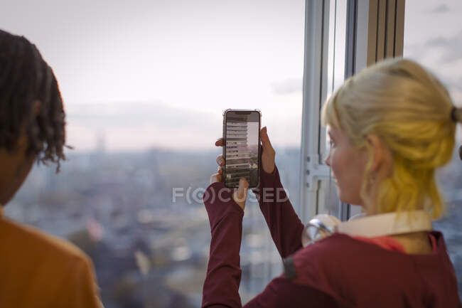 Jovem mulher usando telefone câmera na janela do escritório highrise — Fotografia de Stock