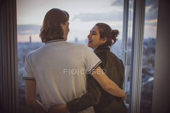 Felice giovane coppia che si abbraccia alla finestra highrise — Foto stock