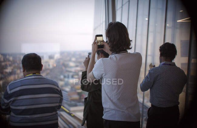 Uomini d'affari che usano i telefoni della fotocamera alla finestra dell'ufficio urbano — Foto stock