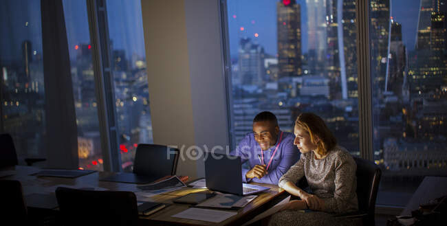 Gente de negocios trabajando hasta tarde en el portátil en la oficina de rascacielos, Londres, Reino Unido - foto de stock