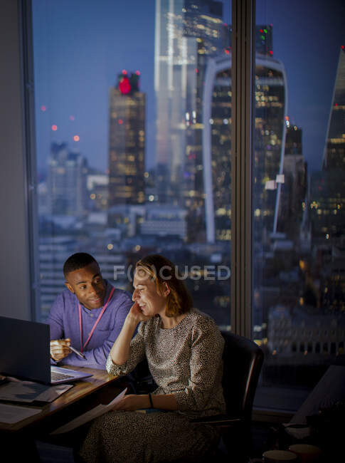 Деловые люди, поздно работающие за ноутбуком в высотном офисе, Лондон, Великобритания — стоковое фото