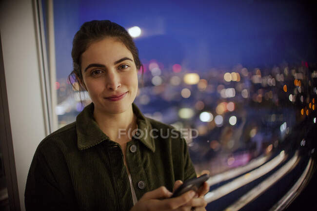 Portrait businesswoman with smart phone at office window at night — Stock Photo