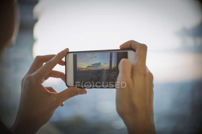 Gros plan femme avec appareil photo téléphone photographie coucher de soleil sur la ville — Photo de stock