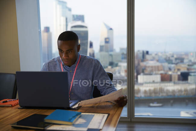 Focused businessman working at laptop in highrise office, London, UK — Stock Photo