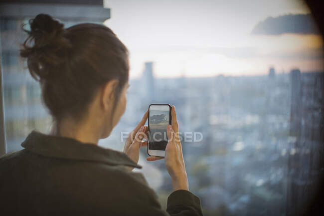 Businesswoman with camera phone photographing sunset over city — Stock Photo