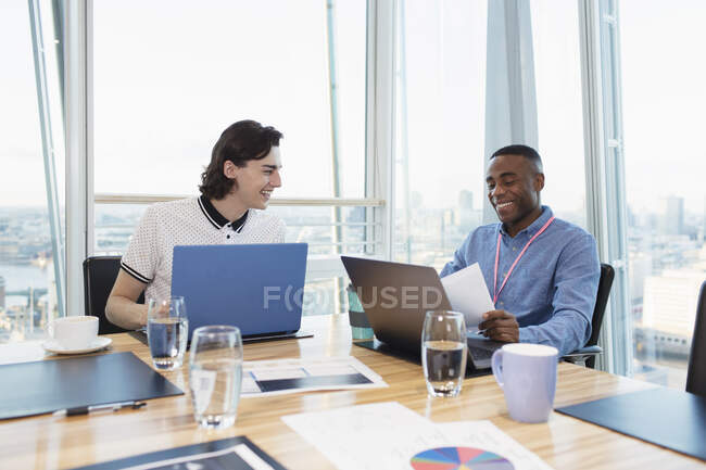 Hombres de negocios sonrientes trabajando en computadoras portátiles en la sala de conferencias Highrise - foto de stock