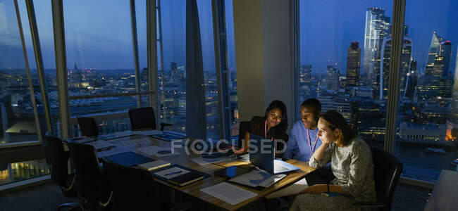 Деловые люди, поздно работающие за ноутбуком в высотном офисе, Лондон, Великобритания — стоковое фото