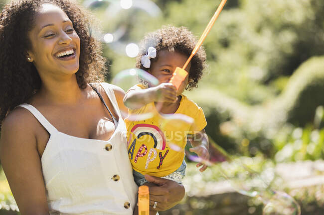Happy mother and toddler daughter playing with bubble wand in sunshine — Stock Photo