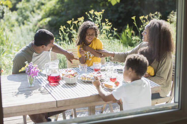 Щаслива сім'я насолоджується обідом на сонячному літньому патіо — стокове фото