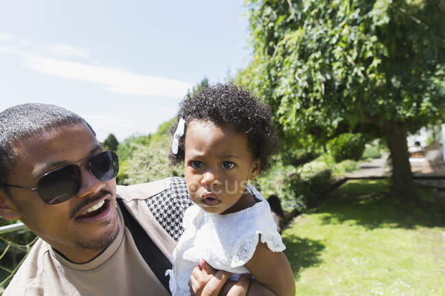 Father holding curious toddler daughter in sunny summer backyard — Stock Photo