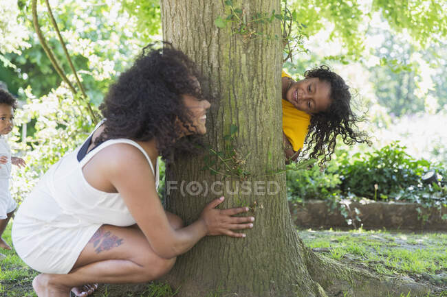 Verspieltes Versteckspiel zwischen Mutter und Tochter am Baum — Stockfoto