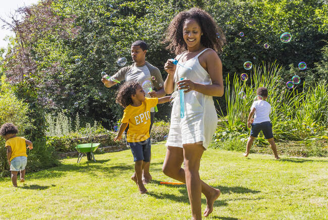 Feliz família brincando e soprando bolhas no ensolarado jardim de verão — Fotografia de Stock