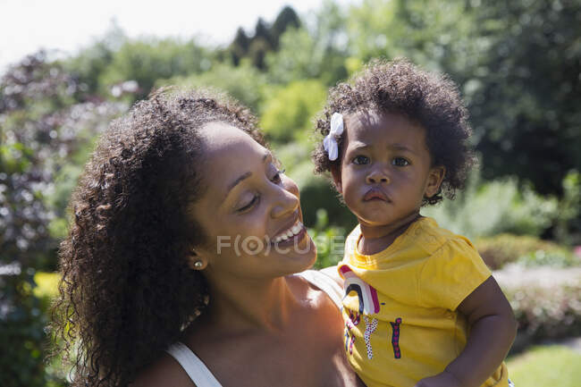 Retrato feliz madre holding lindo niño hija en sunny patio - foto de stock