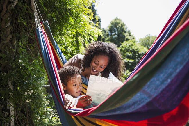 Mãe e filho lendo livro na ensolarada rede de verão no quintal — Fotografia de Stock