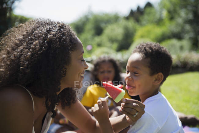 Playful mother and son eating watermelon popsicles on sunny patio — Stock Photo