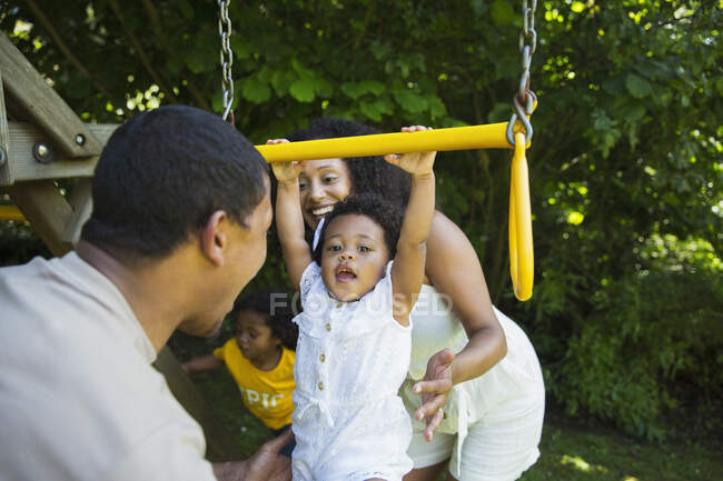 Parents watching happy toddler daughter hanging from swing — Stock Photo