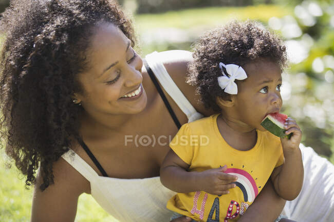 Glückliche Mutter beobachtet Kleinkind-Tochter beim Wassermelonenessen — Stockfoto