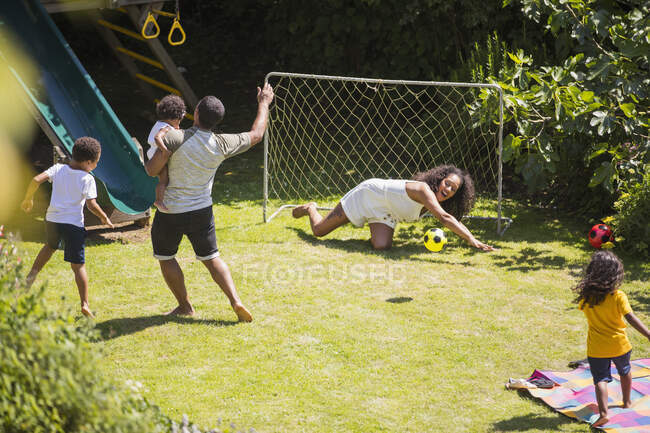 Família feliz jogando futebol no quintal ensolarado do verão — Fotografia de Stock
