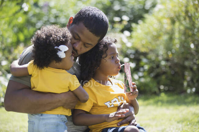 Прихильний батько обіймає дочок на сонячному літньому подвір'ї — стокове фото