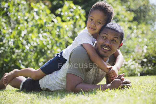 Retrato afectuoso padre e hijo tendidos en la hierba soleada de verano - foto de stock